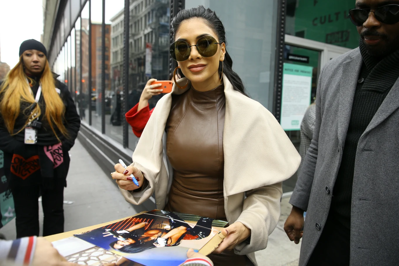 Nicole Scherzinger niejednokrotnie opowiadała o swojej diecie w mediach Kobieta w brązowej sukience i jasnym płaszczu podpisuje zdjęcia dla fanów na ulicy, nosi duże okulary przeciwsłoneczne i uśmiecha się, wokół niej stoją inne osoby.
