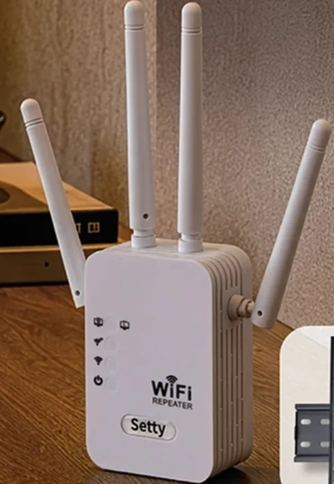 Wzmacniacz sygnału Biały wzmacniacz sygnału WiFi marki Setty wyposażony w cztery anteny, umieszczony na drewnianym blacie obok ściany.