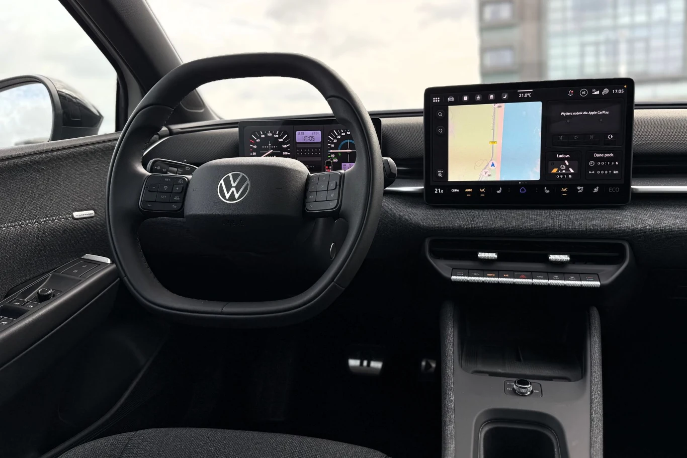 Kierownica z logo Volkswagena, cyfrowe zegary i nowoczesny ekran systemu multimedialnego z widoczną nawigacją oraz dotykowy panel sterowania w centralnej części kokpitu.