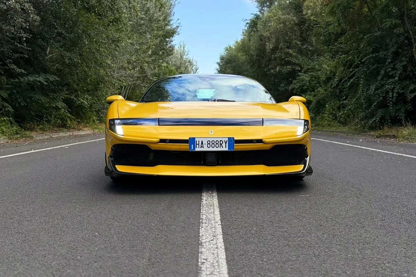 Ferrari 849 Testarossa mocno czerpie ze swojego dziedzictwa - kanciasty przód przywołuje mi na myśl 288 GTO czy 308 GTS. Żółty sportowy samochód zaparkowany na środku pustej asfaltowej drogi otoczonej zielenią.