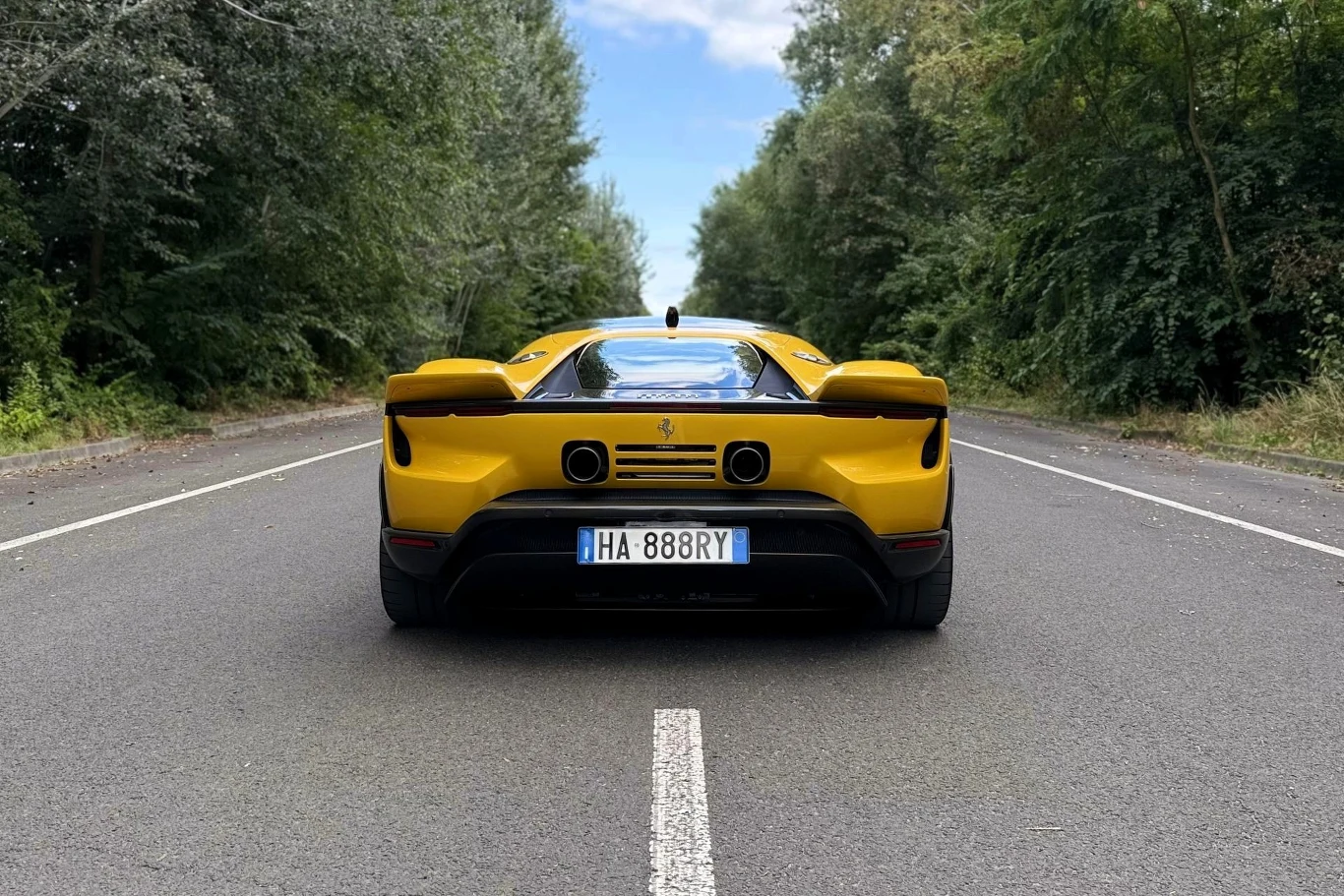 Na rozpędzenie się od 0 do 100 km/h Ferrari 849 Testarossa potrzebuje mniej niż 2,3 s. Prędkość maksymalna to ponad 330 km/h. żółty supersamochód Ferrari zaparkowany centralnie na pustej asfaltowej drodze, otoczony zielenią po bokach