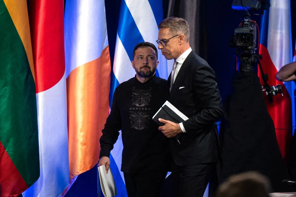 Wołodymyr Zełenski i prezydent Finlandii Alexander Stubb podczas szczytu tzw. koalicji chętnych Dwóch mężczyzn idących obok siebie na tle flag różnych państw, jeden z nich trzyma dokumenty, drugi notatnik.