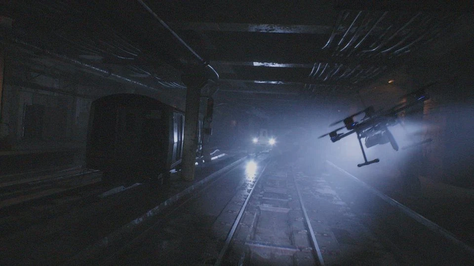 Opuszczony tunel metra z ciemnym pociągiem po lewej stronie i dronem unoszącym się w świetle reflektorów po prawej, tworzący atmosferę tajemnicy i napięcia.