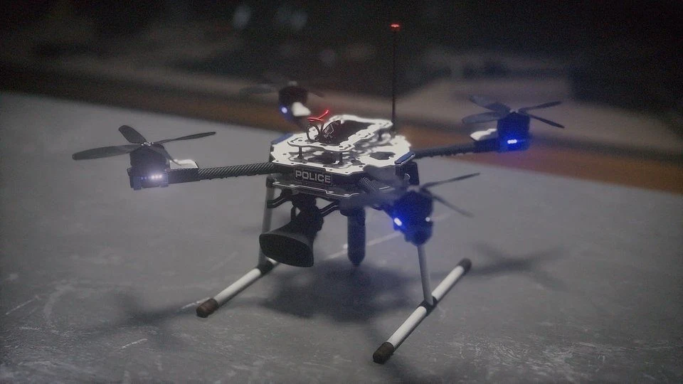 Policyjny dron z czterema śmigłami, reflektorami LED oraz zamontowanymi kamerami, stojący na stole o ciemnej powierzchni.