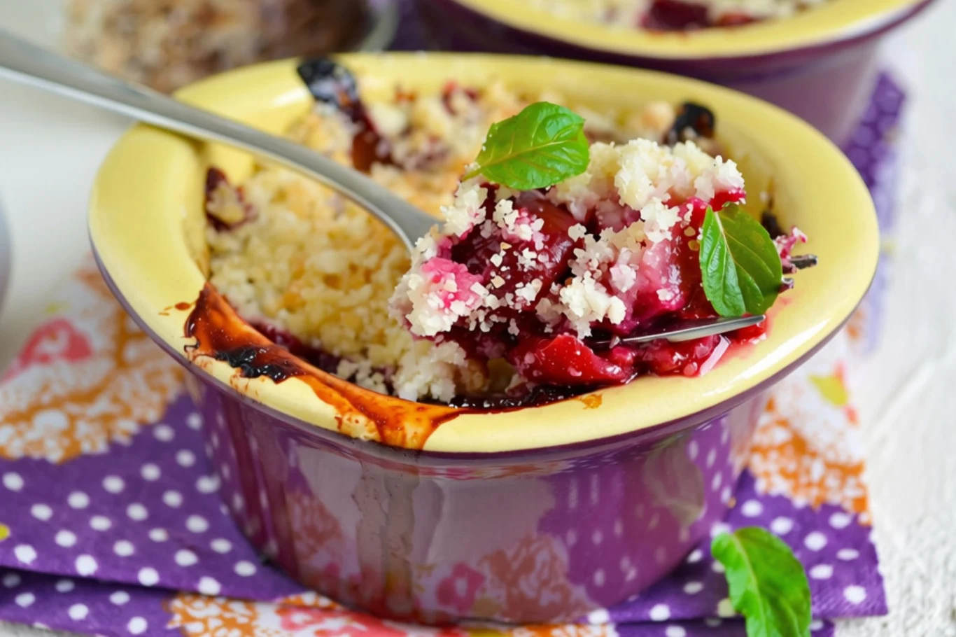 Crumble ze śliwkami to najlepszy jesienny deser Crumble ze śliwkami w ceramicznej foremce, chrupiąca kruszonka, dekoracja ze świeżej mięty, porcja nabierana łyżką