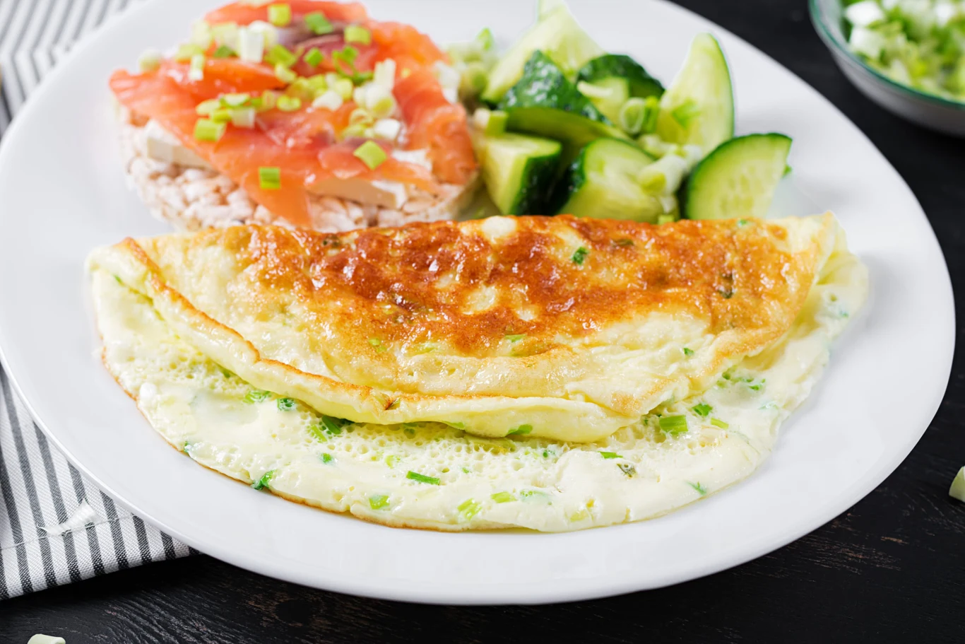 Puszysty omlet Złocisty omlet z delikatną szczypiorkową posypką, plasterki łososia na chrupiących waflach ryżowych oraz świeże kawałki ogórka.