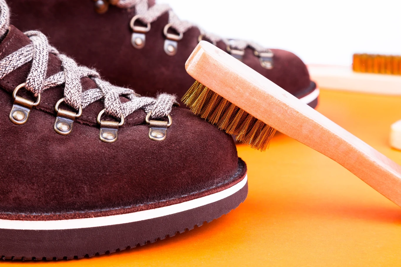 Bordowe buty trekkingowe z jasnymi sznurowadłami, czyszczone szczotką o jasnym drewnianym uchwycie i brązowym włosiu.
