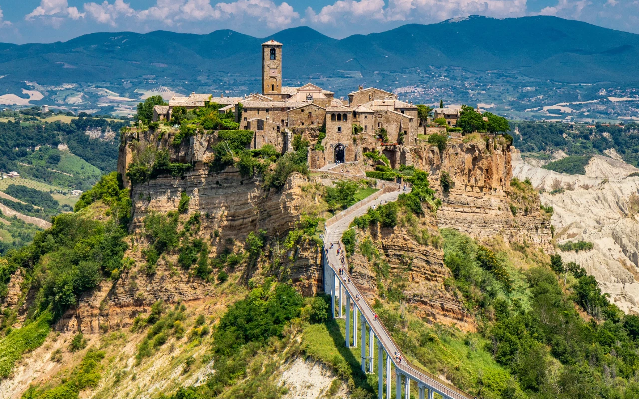 Civita di Bagnoregio Civita di Bagnoregio wzniesione na malowniczym wzgórzu, otoczone zielenią i połączone ze światem długą, wąską kładką.