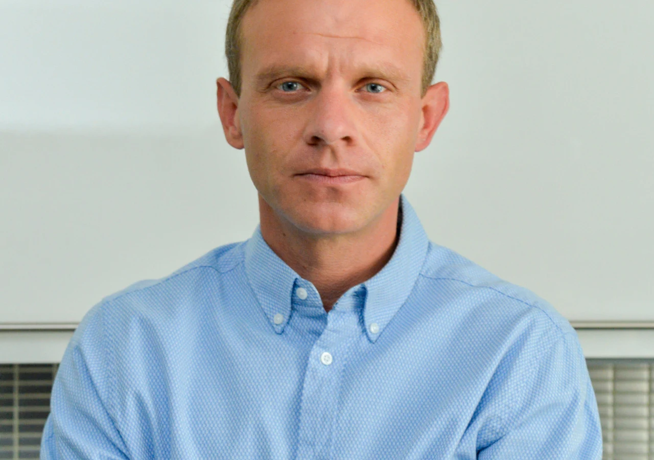 Kazimierz Mazur Mężczyzna o jasnych włosach i jasnych oczach w niebieskiej koszuli z zapiętym kołnierzykiem, patrzący prosto przed siebie z poważnym wyrazem twarzy.