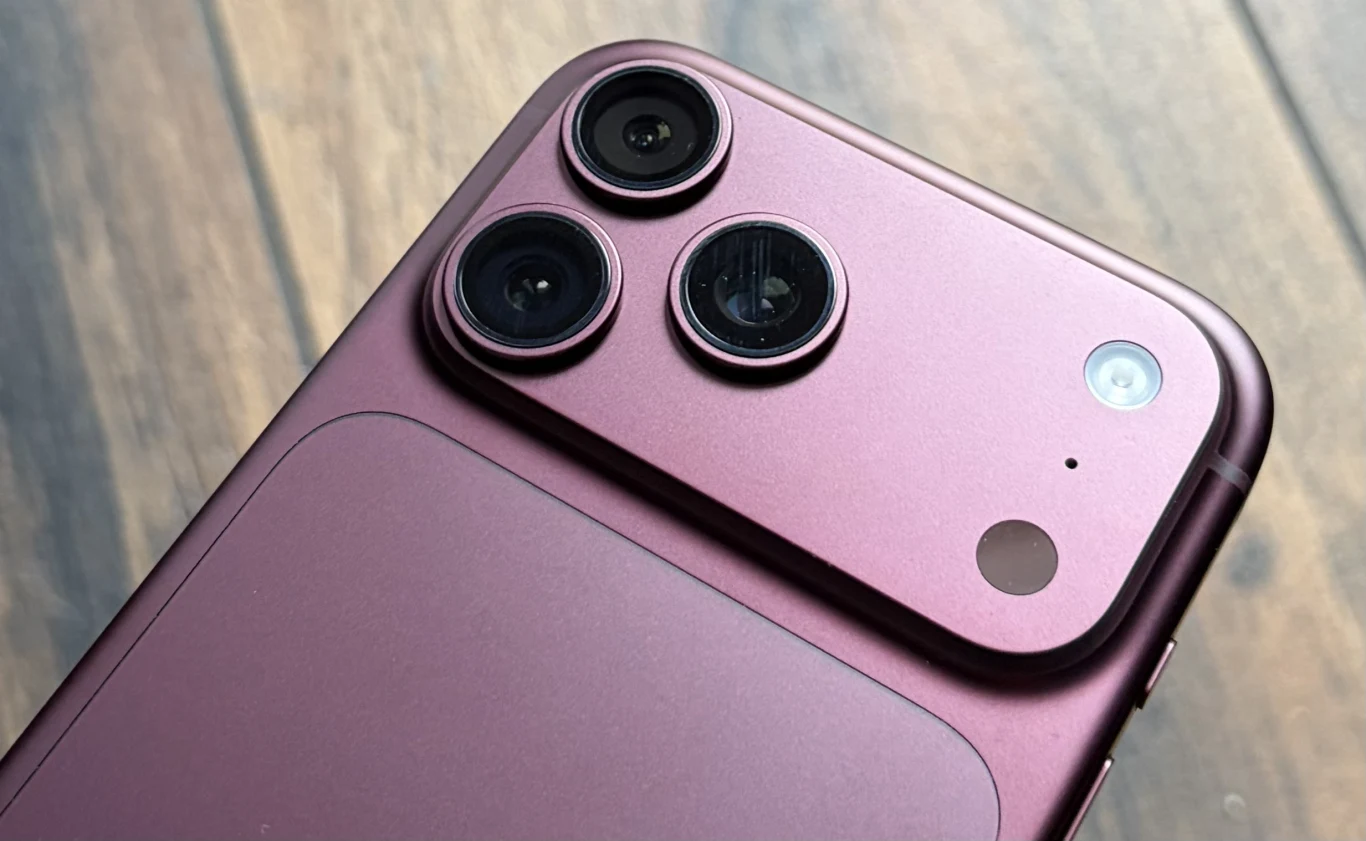 iPhone 18 Pro Max. Pierwsze wrażenia i zapowiedź recenzji. Moduł aparatu iPhone 18 Pro Max w kolorze burgundu z trzema soczewkami i lampą na tle drewna.
