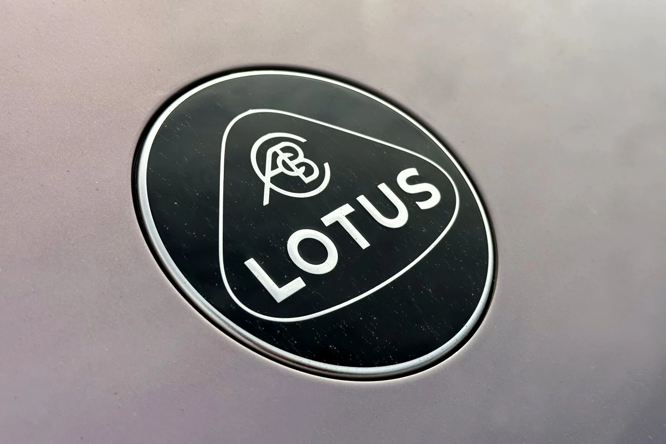 Ceny Lotusa Eletre zaczynają się od ok. 430 tys. zł. Czarne, owalne logo firmy Lotus z białym napisem i stylizowanymi inicjałami w górnej części znaku.