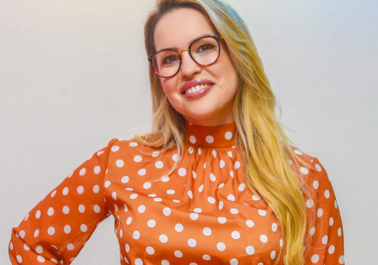 Julia Oleś Julia Oleś w okularach i pomarańczowej sukience w białe grochy. Ma długie blond włosy opadające na jedno ramię.
