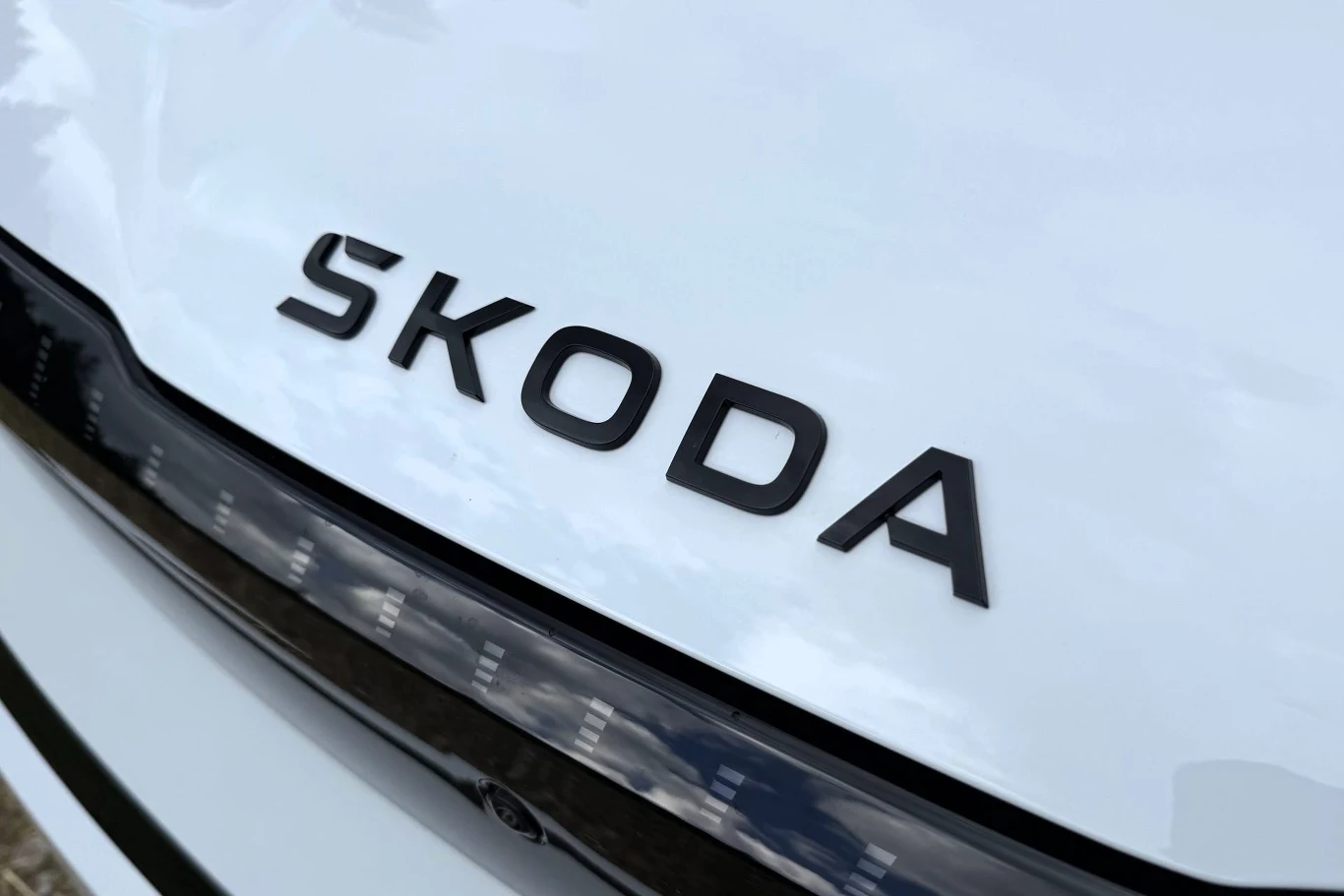 Skoda Peaq dostępna jest w trzech wariantach mocy: 204, 286 i 299 KM. Czarne litery napisu ŠKODA na białej masce samochodu tuż nad reflektorem.
