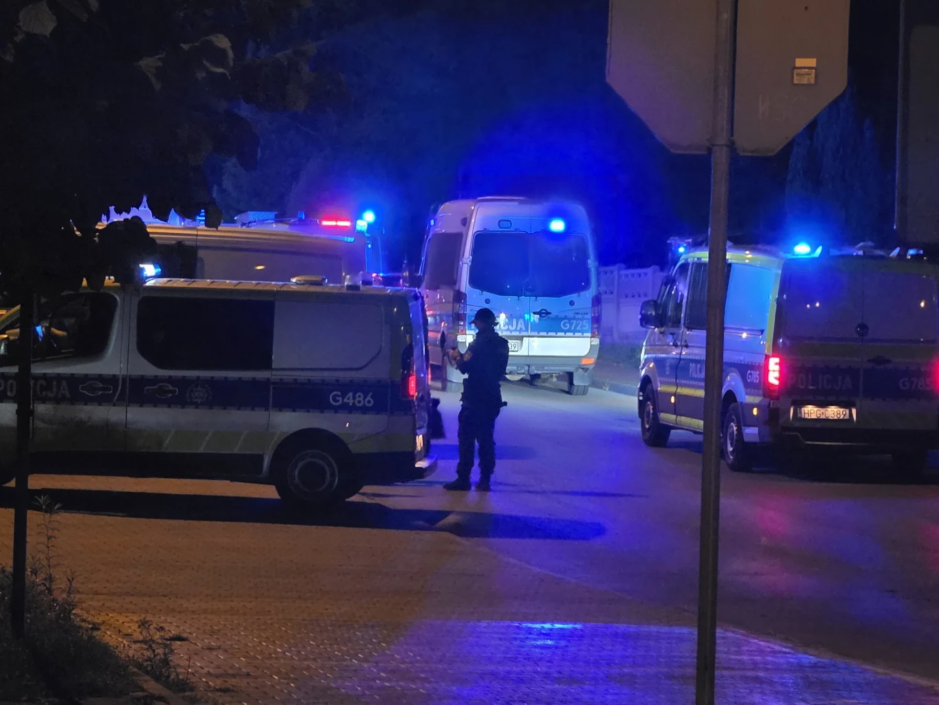 Strzelanina w Bukownie Radiowozy policyjne z włączonymi sygnałami świetlnymi i policjant na ulicy w Bukownie nocą.