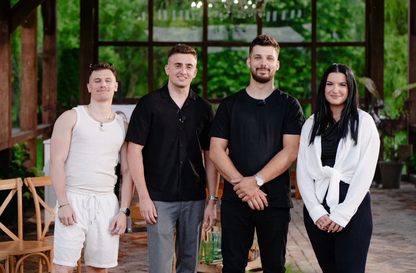 "Rolnik szuka żony" Uczestnicy programu 'Rolnik szuka żony' stojący w drewnianej altanie z dużymi oknami, w tle zieleń.