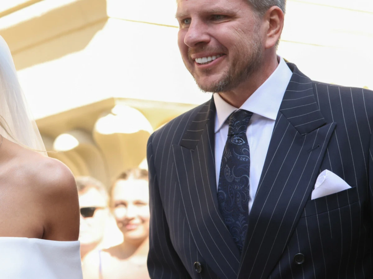 Filip Chajzer wziął ślub Elegancki mężczyzna w ciemnym, prążkowanym garniturze z białą poszetką i ozdobnym krawatem, stojący obok osoby w białej sukni ślubnej.