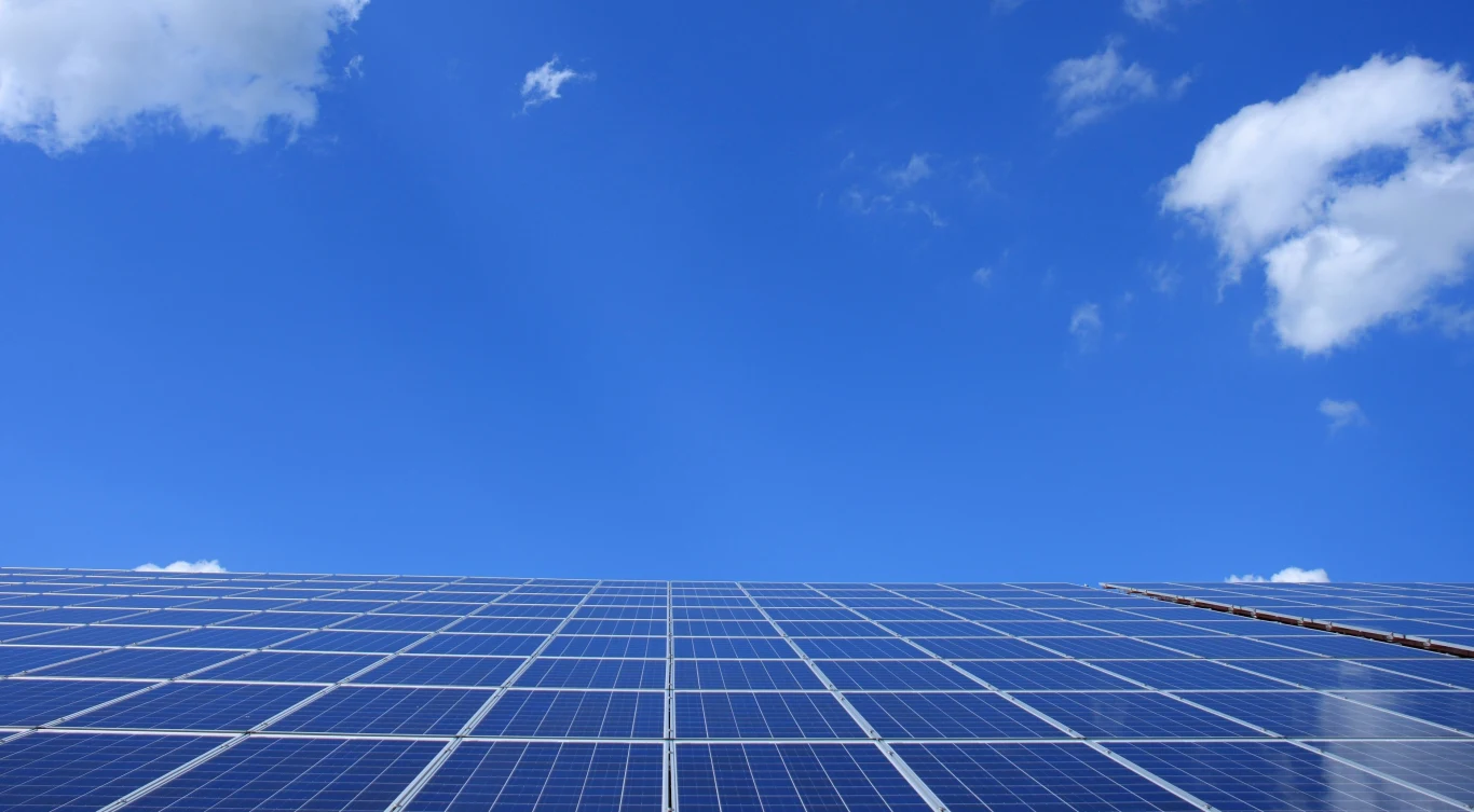 W 2025 roku czysta energia stanowiła 26,2 proc. końcowego zużycia, a obecne plany krajowe prowadzą do około 41 proc. w 2030 r. przy obowiązującym celu 42,5 proc. Rząd paneli fotowoltaicznych pod jasnym niebem, symbolizujący wzrost udziału OZE w zużyciu energii.