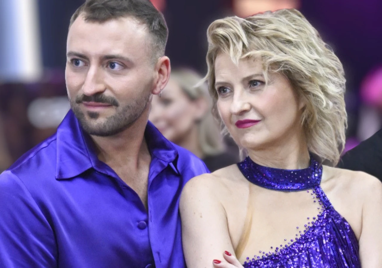 Dwoje dorosłych w zbliżeniu, ubranych w fioletowe, eleganckie stroje, patrzących w lewą stronę kadru.