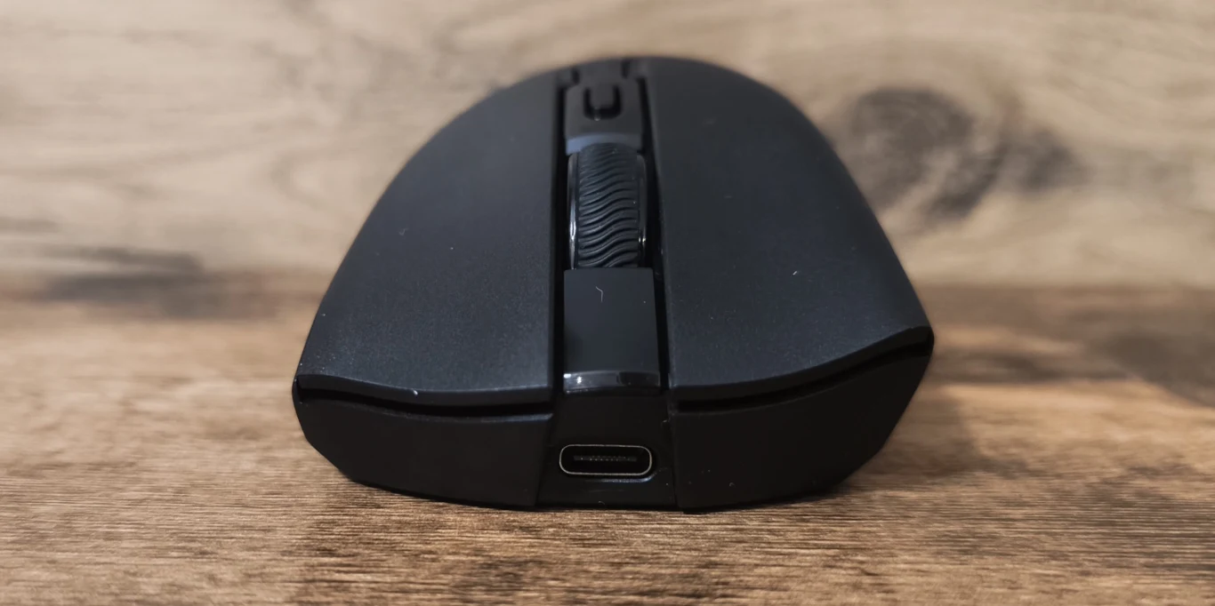 Czarna bezprzewodowa mysz komputerowa z wyraźnie widocznym scrollowanym kółkiem i portem USB-C ustawiona na drewnianej powierzchni.