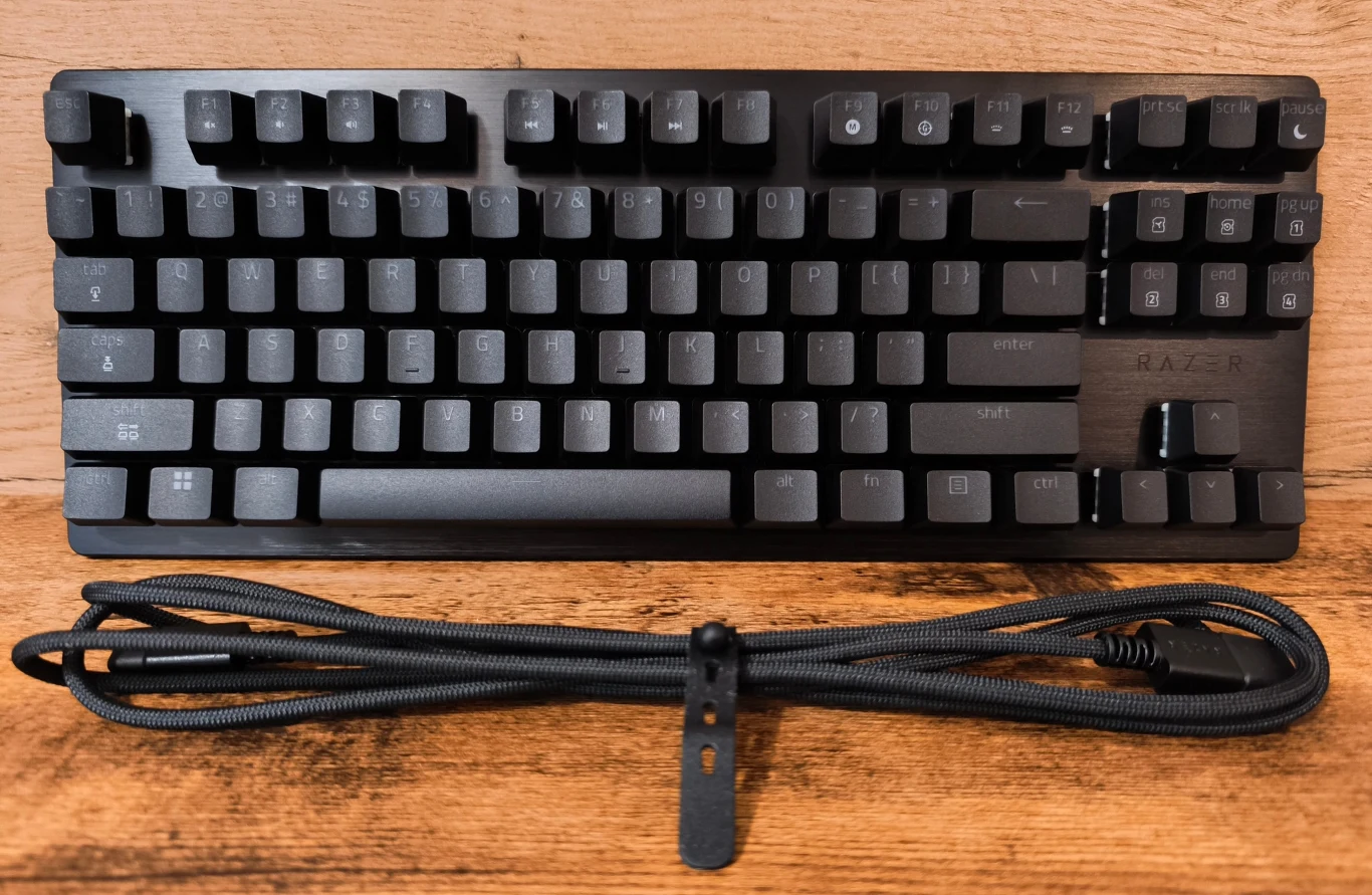 Czarna mechaniczna klawiatura Razer z wytrzymałym oplecionym przewodem USB ułożonym z przodu na drewnianym blacie.