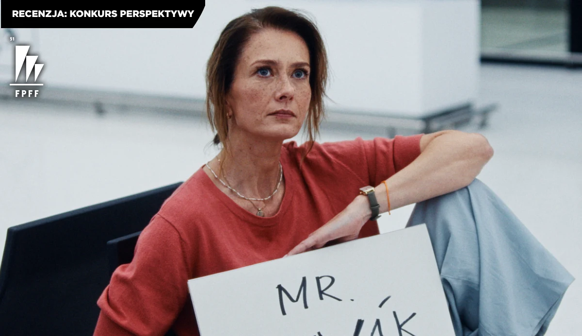 Anita Sokołowska w filmie "Miłe kobiety" Anita Sokołowska w czerwonej bluzie siedzi na podłodze i trzyma tabliczkę z napisem „MR.”