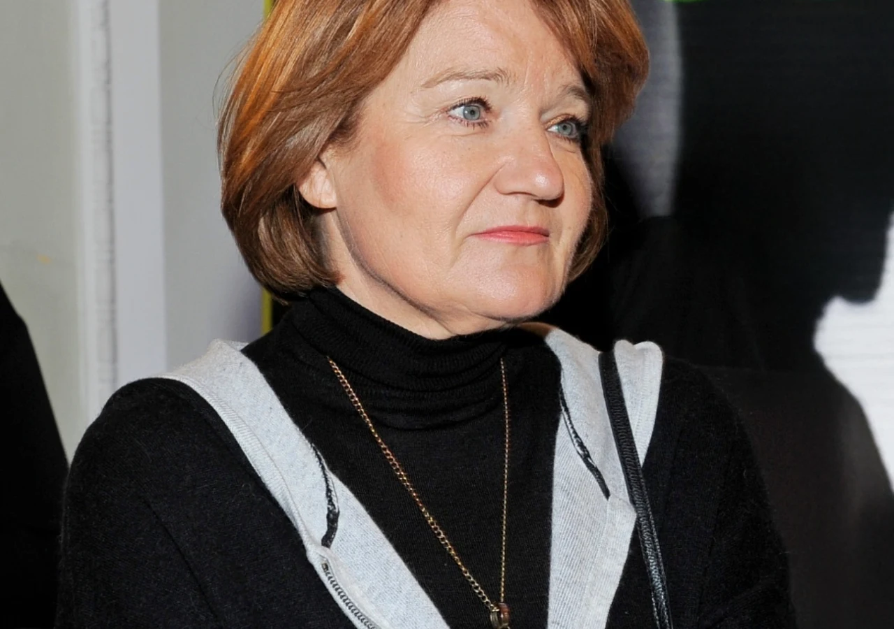Maria Winiarska Aktorka Maria Winiarska z rudymi włosami, w czarnym golfie i jasnoszarej bluzie, patrząca w bok.