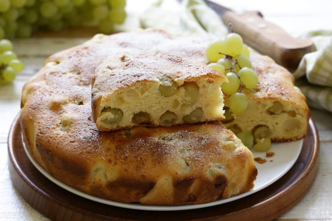 Słodka focaccia z winogronami. Włosi zajadają się nią jesienią Słodka focaccia z winogronami, przekrojona, pokazująca owoce w środku, leży na drewnianej desce, udekorowana winogronami.