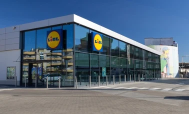  Przeszklony, wolnostojący sklep Lidl z dwoma logo sieci na fasadzie w słoneczny dzień