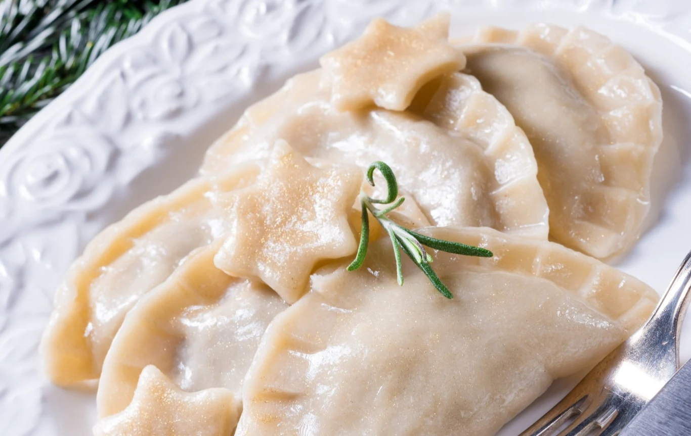 Te pierogi smakują wyjątkowo nie tylko w święta Pierogi z kapustą i grzybami oraz pierożki w kształcie gwiazdek i gałązka rozmarynu na białym talerzu.