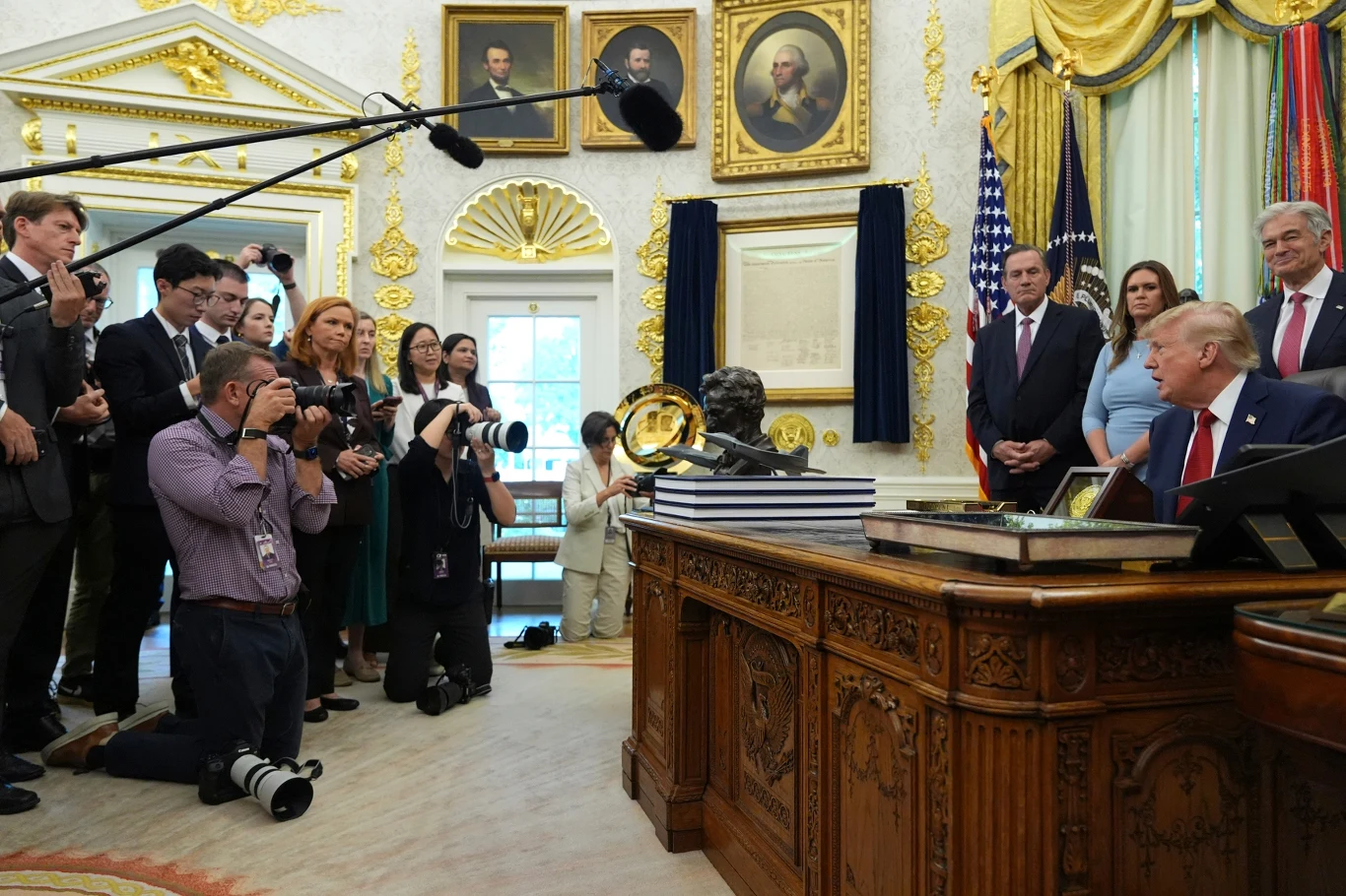 Donald Trump kocha blask fleszy, ale prowadzi wojnę z mediami, które go krytykują Donald Trump przy biurku w gabinecie, otoczony doradcami i dziennikarzami z aparatami i kamerami.