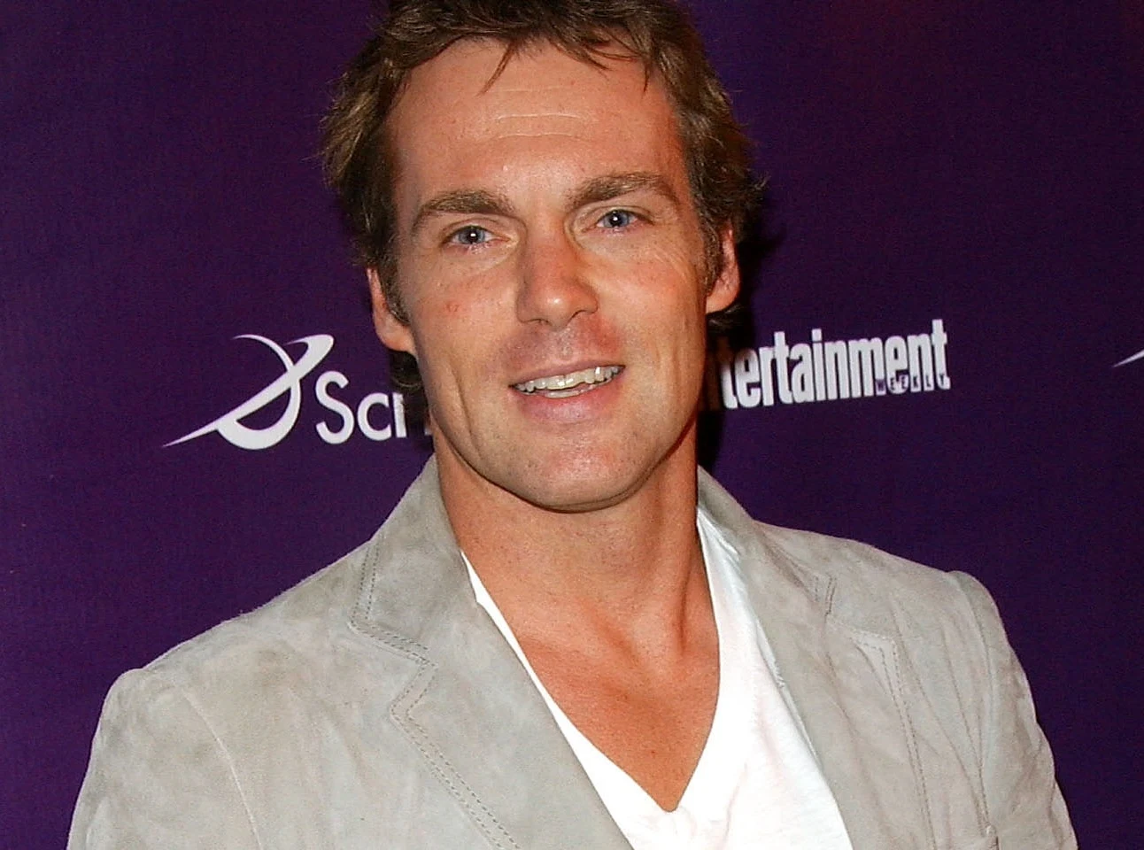 Michael Shanks Michael Shanks w jasnej marynarce i białej koszulce na tle ścianki z logo SciFi i Entertainment