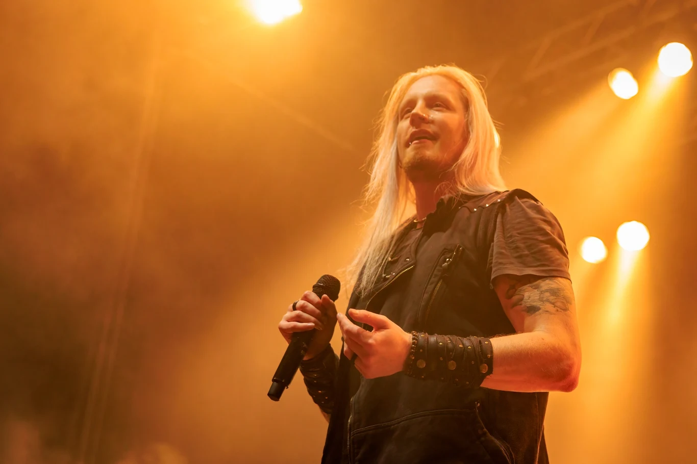 Marc Hudson do DragonForce dołączył w 2011 r. Marc Hudson z DragonForce, długie blond włosy, tatuaż na ramieniu, śpiewa do mikrofonu na scenie.