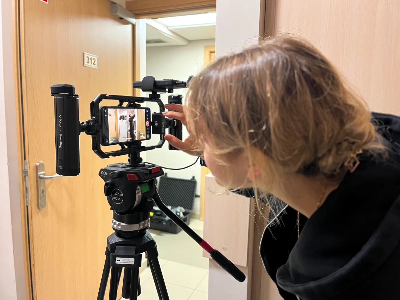 „Vivo odkryłam będąc w Tajlandii szukając nowego telefonu dobrego do tworzenia treści na social media” mówi Joanna Cichoń, zwyciężczyni konkursu vivo Creators Club Osoba ustawiająca smartfon zamocowany na statywie w korytarzu budynku, skoncentrowana na precyzyjnym kadrowaniu ujęcia.