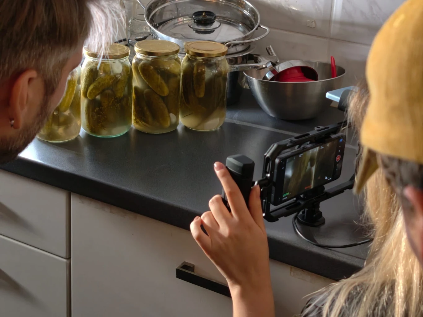 „Chyba wszyscy, których znam, robią przetwory” mówi Joanna Słoiki z ogórkami konserwowymi ustawione na kuchennym blacie, uchwycone przez osobę nagrywającą film aparatem ustawionym na statywie, obok widoczne metalowe naczynia.
