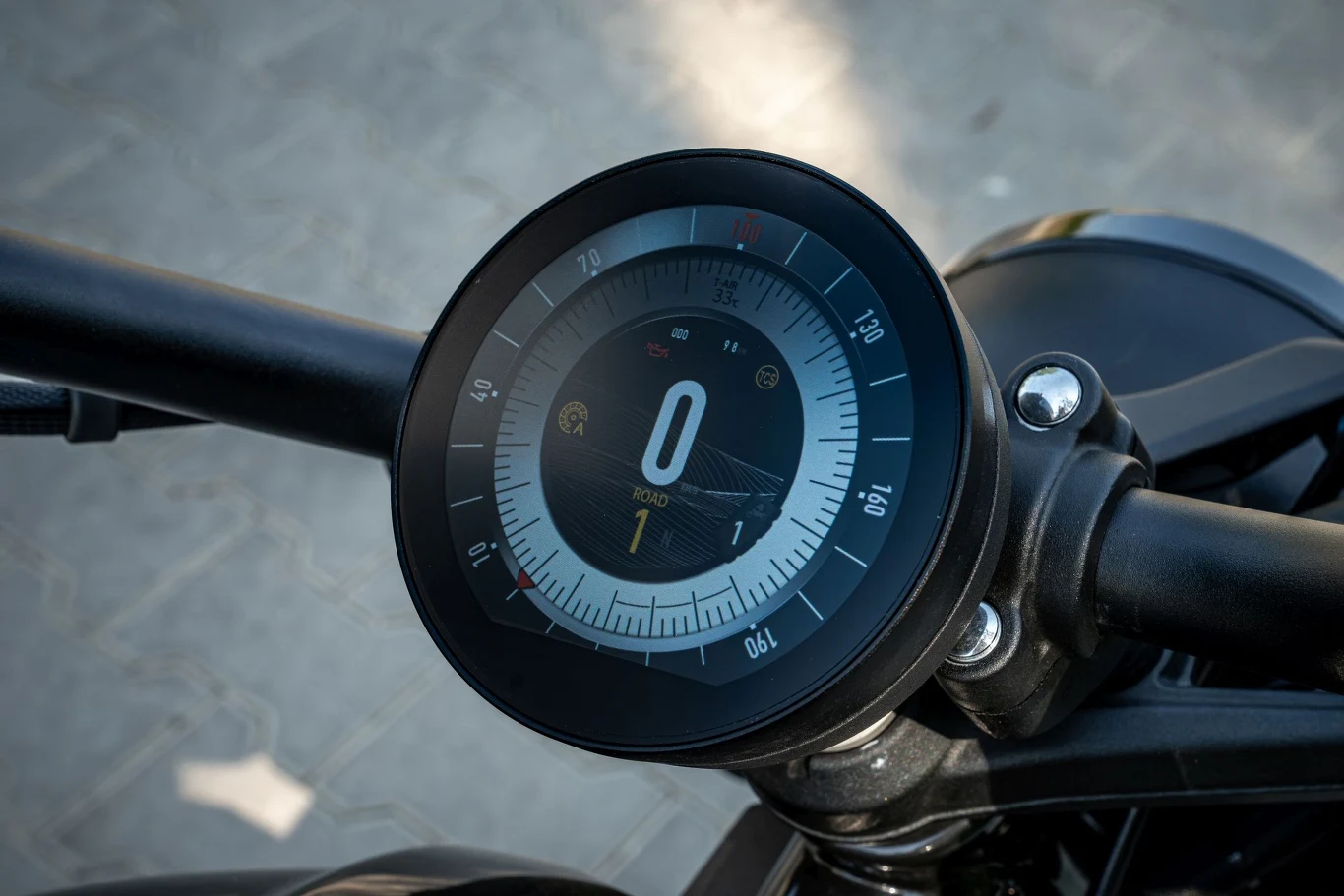 Cyfrowy prędkościomierz motocykla z wyraźnie widocznym wskazaniem prędkości zero i trybu jazdy ROAD na tle czarnych elementów kierownicy.
