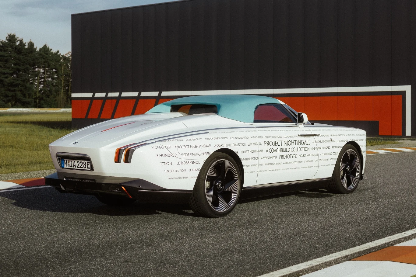 luksusowy biały roadster z niebieskim dachem, designerskie felgi, nowoczesne tylne światła, geometria nadwozia podkreślona napisem Project Nightingale, samochód ustawiony na torze wyścigowym przy czarno-czerwonej ścianie