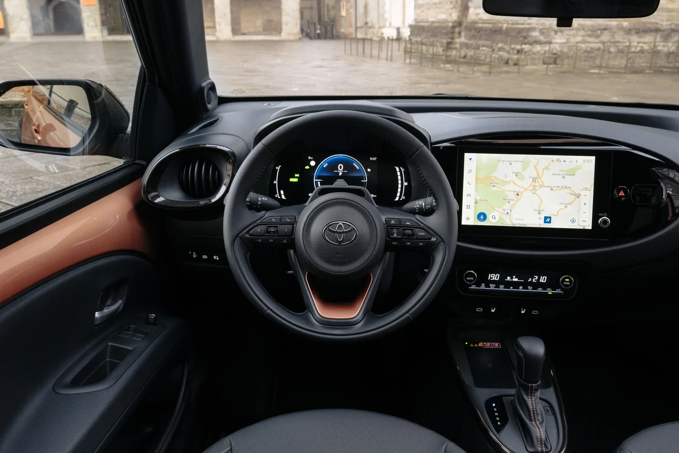 Wnętrze samochodu marki Toyota z widoczną kierownicą, cyfrowym zestawem wskaźników oraz dużym ekranem dotykowym na konsoli środkowej wyświetlającym mapę nawigacji.
