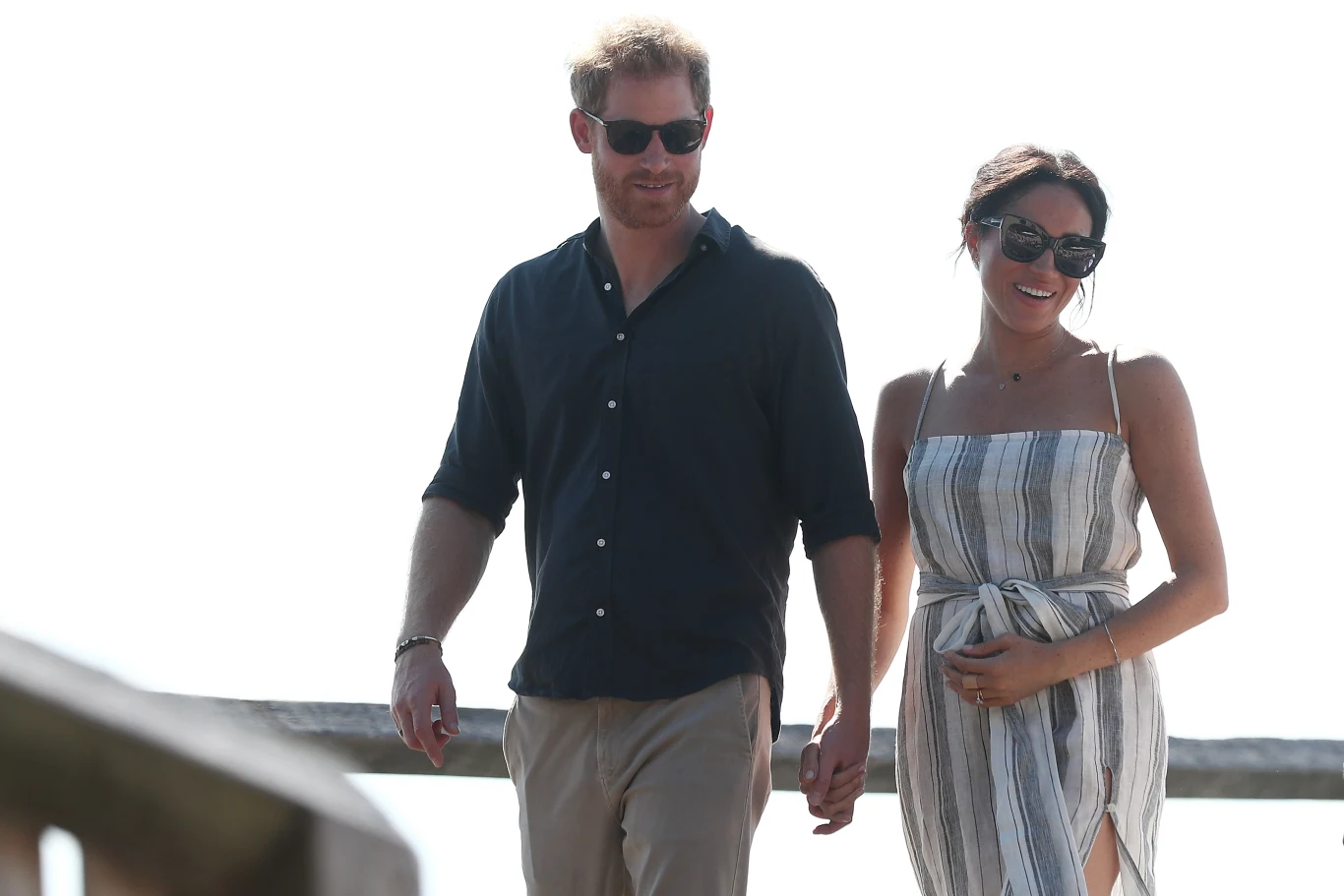 Meghan Markle postanowiła zostać w Wielkiej Brytanii i wygląda na to, że pobyt tam nie jest dla niej "karą" Para ubrana w letnie stroje spaceruje razem, trzymając się za ręce, w słoneczny dzień, oboje noszą ciemne okulary przeciwsłoneczne.