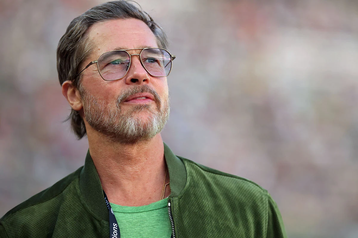 Brad Pitt Brad Pitt w zielonej kurtce i okularach, z krótkimi siwiejącymi włosami i zarostem, na rozmytym tle.