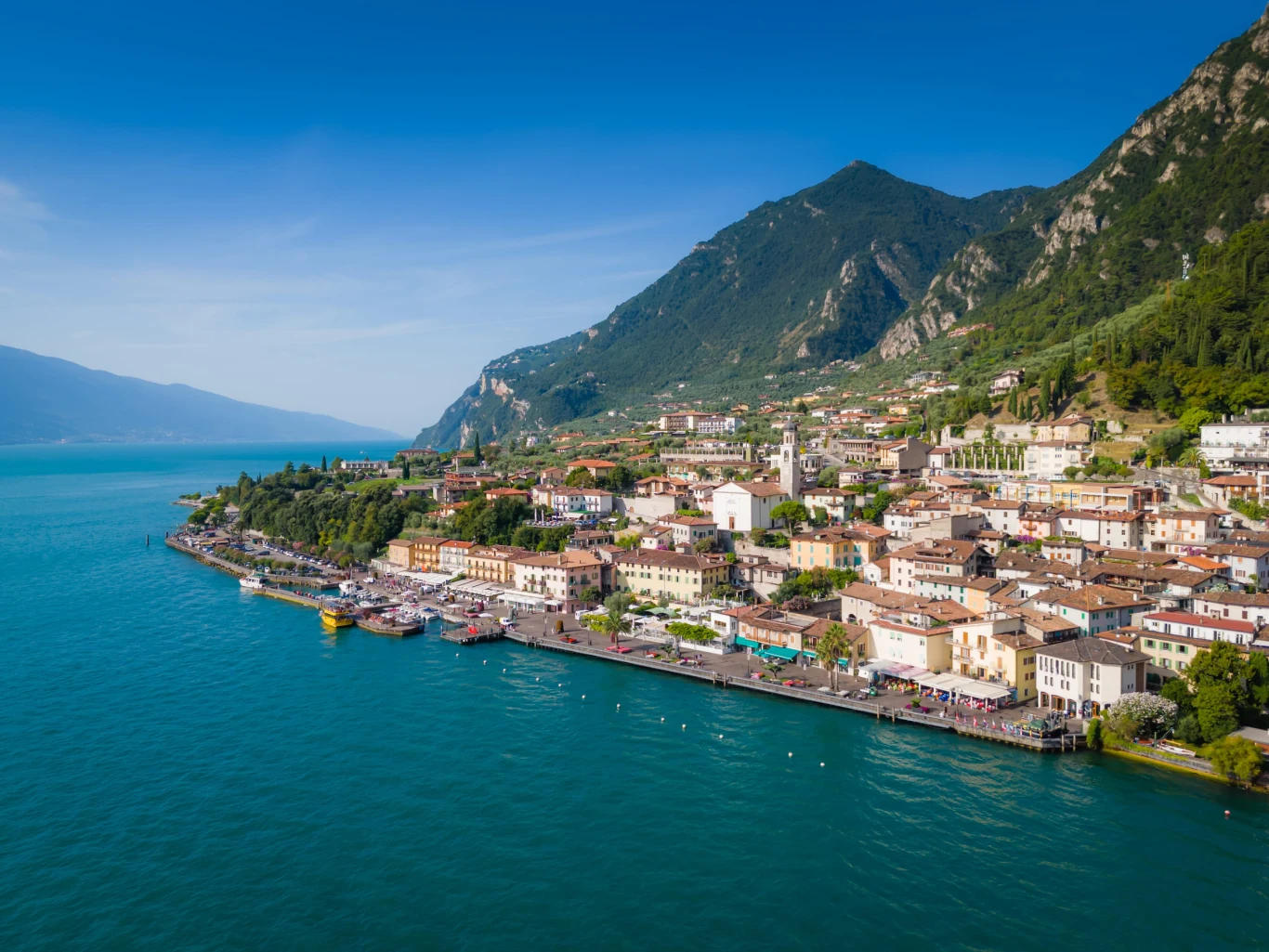Limone sul Garda to jedna z najpiękniejszych miejscowości nad włoskim jeziorem Malownicze miasteczko położone nad jeziorem, otoczone zielonymi wzgórzami i górami, z promenadą wzdłuż brzegu oraz zwartą zabudową w jasnych kolorach.