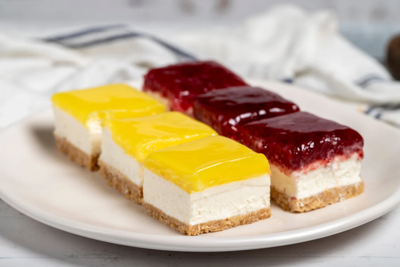Sernik lemon curd to apetyczny deser dla fanów orzeźwiającego smaku cytryny Cztery kawałki sernika lemon curd na spodzie z herbatników, dwa z żółtą galaretką cytrynową, dwa z czerwoną galaretką.