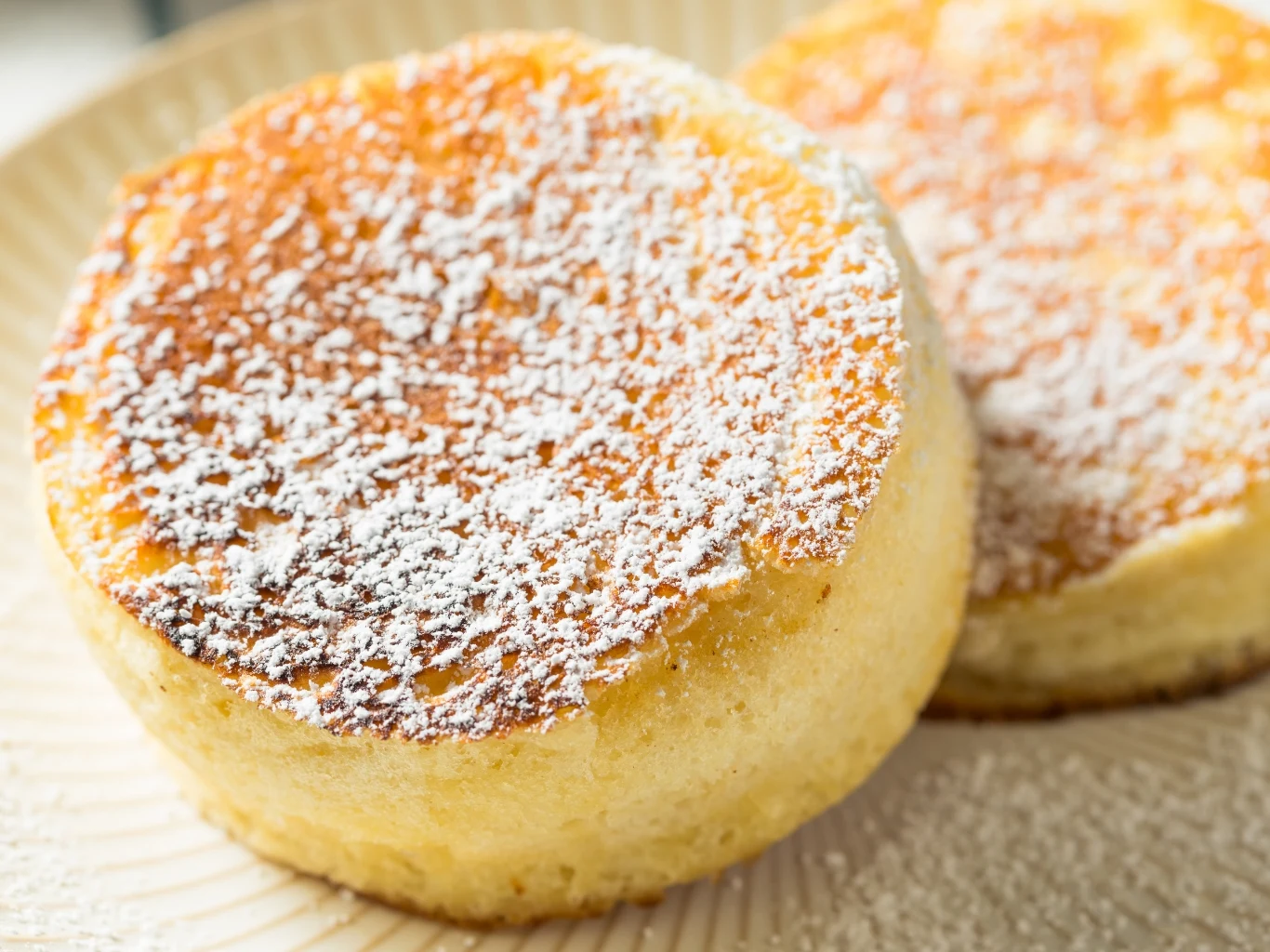 Puszyste naleśniki japońskie to dobra propozycja na śnadanie lub obiad na słodko. Dwa puszyste japońskie pancakes posypane cukrem pudrem na jasnym talerzu.