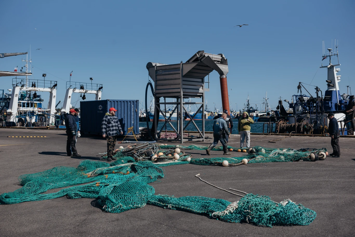 Port we Władysławowie zmienia swoją funkcję z czysto rybackiej na gospodarczo-turystyczną Grupa rybaków pracujących przy dużych zielonych sieciach rozłożonych na betonowej powierzchni portu, w otoczeniu kutrów i sprzętu rybackiego.