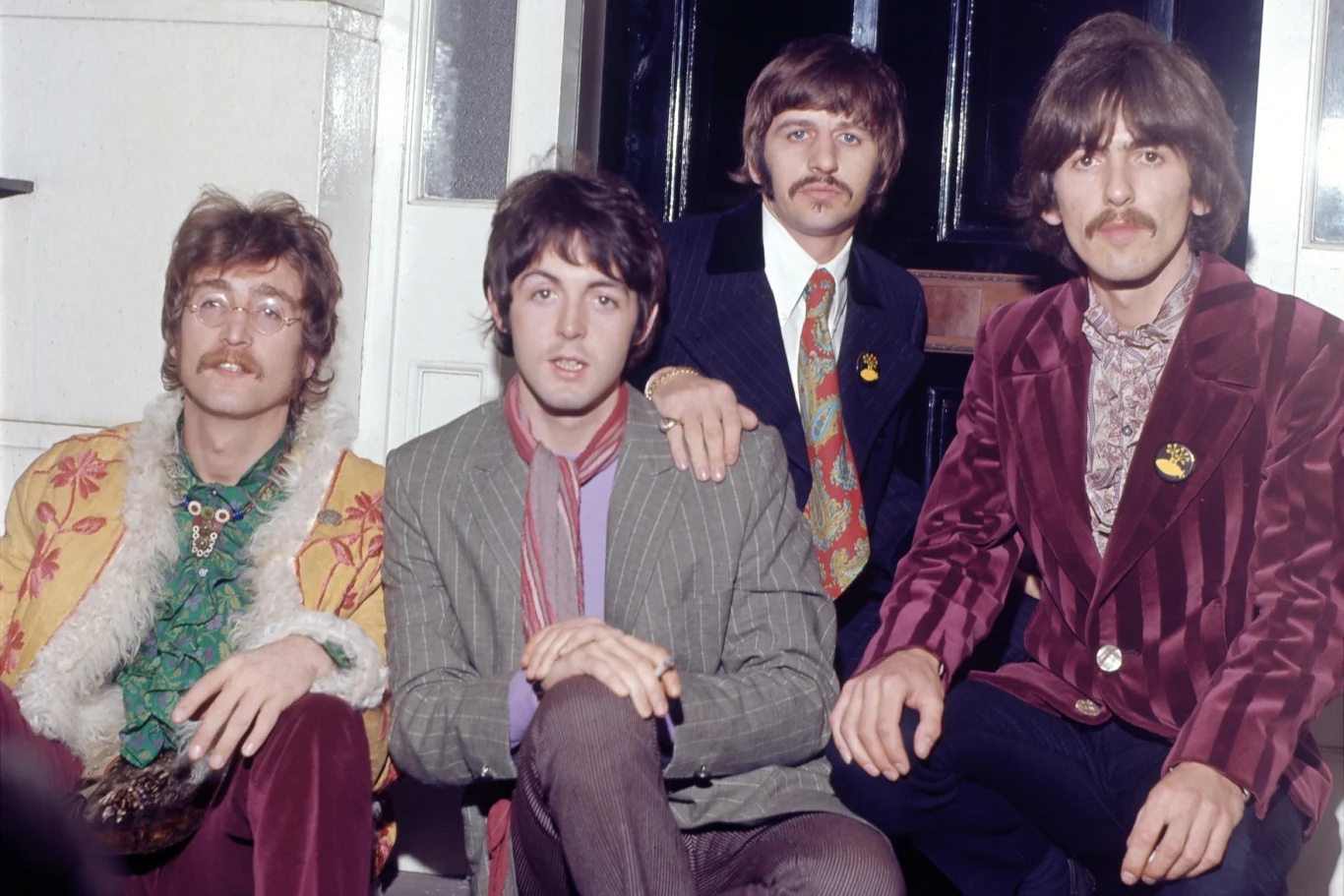 Zespół The Beatles w 1967 r. Czterech członków The Beatles w 1967 roku, ubrani w kolorowe stroje z lat 60., siedzą obok siebie.
