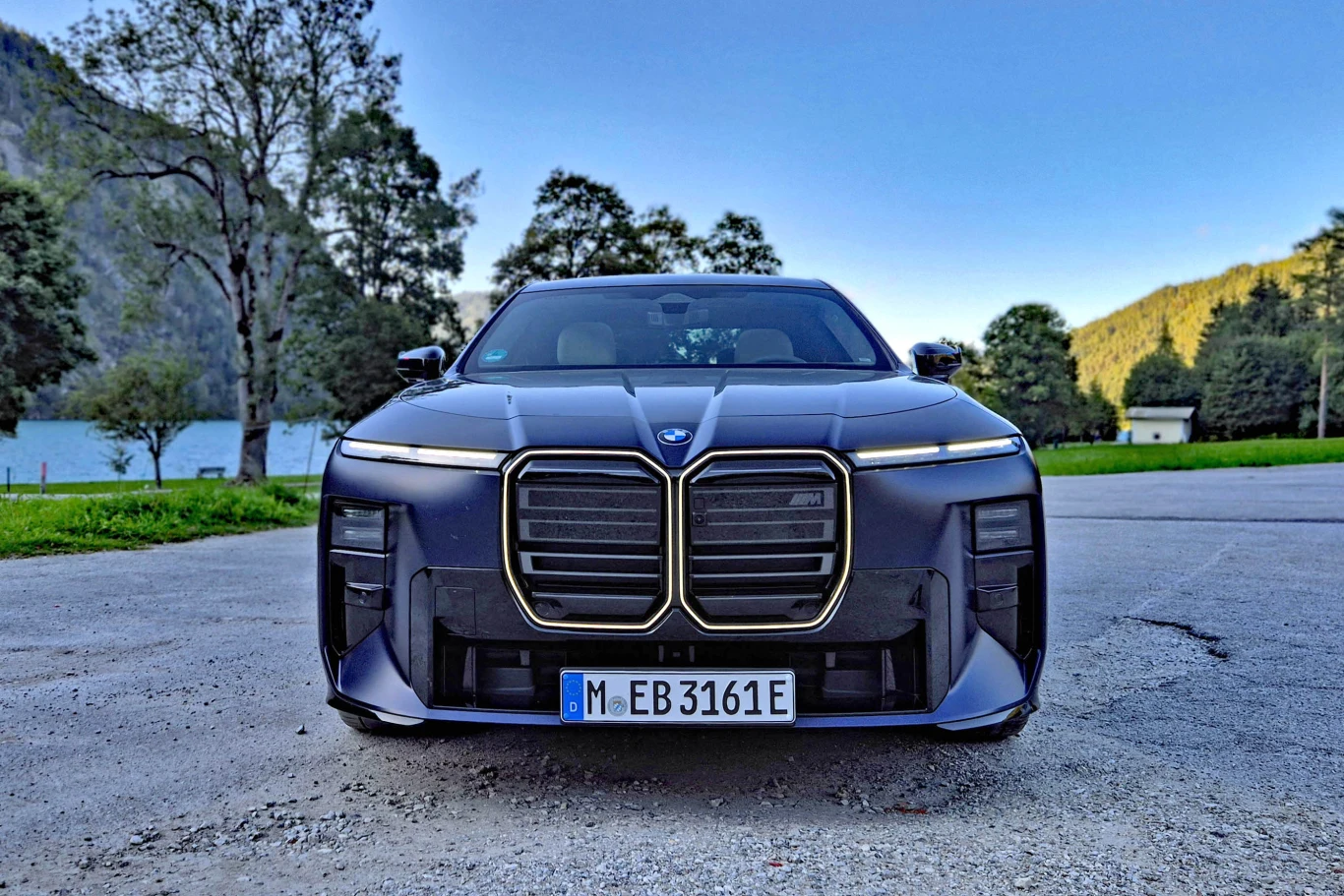 Jose Casas, stylista odpowiedzialny za modernizację BMW serii 7, przekonuje, że przód odświeżonej "siódemki" nadal ma w sobie wiele z dziedzictwa marki, ale jednocześnie jest bardziej subtelny niż w poprzedniku Nowoczesny samochód BMW z charakterystycznym dużym grillem i agresywną linią przednią na parkingu w otoczeniu zieleni oraz górskiego krajobrazu.