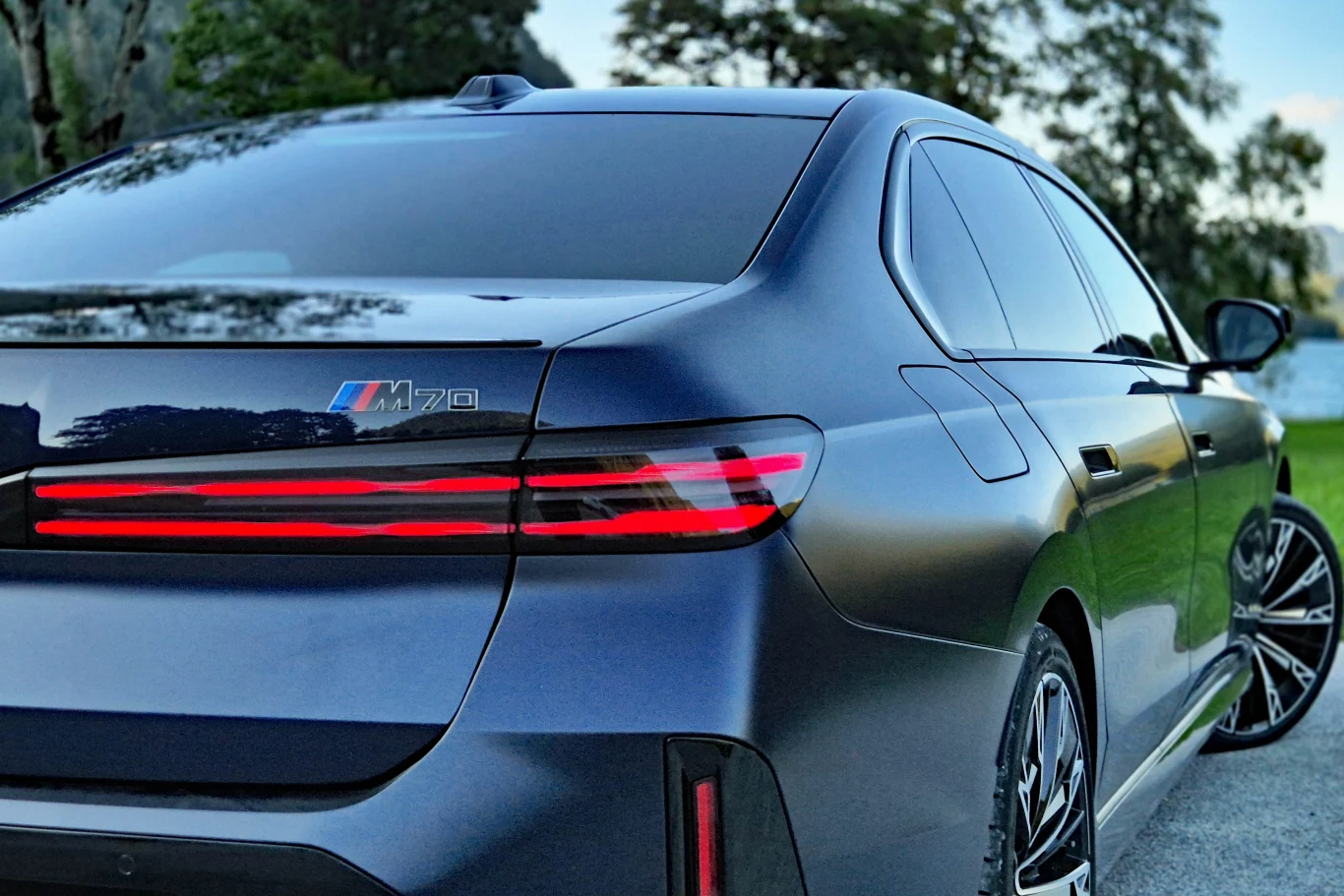 680-konne i7 M70 to najmocniejsza i najszybsza wersja zmodernizowanej serii 7 Tylny fragment czarnego BMW M70 z charakterystycznymi, poziomymi światłami LED oraz oznaczeniem modelu na klapie bagażnika, widoczne sportowe felgi.