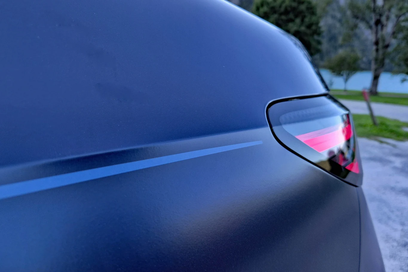 Fakt, że górna i dolna część nadwozia pokryte są różnymi lakierami, podkreśla kontrastująca linia, niczym w Rolls-Royce Zbliżenie na tylną część samochodu z wyraźnie widocznym tylnym światłem i matowym wykończeniem karoserii, przez które biegnie subtelny, poziomy pasek ozdobny.