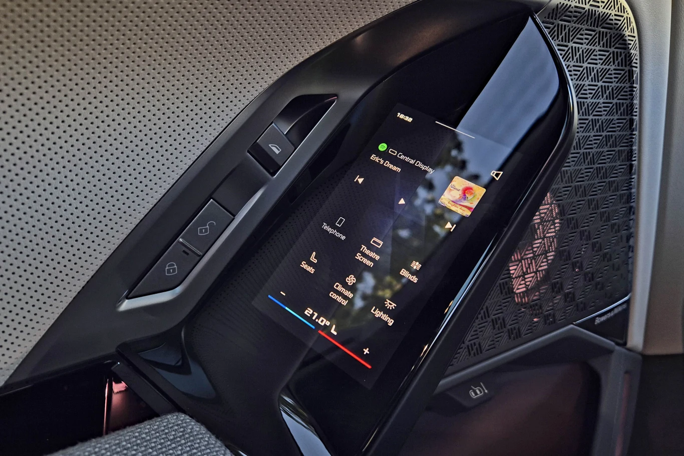 BMW i7 M70 Dotykowy panel sterowania w samochodzie z wyświetlaczem multimedialnym umożliwiającym m.in. sterowanie muzyką oraz kilkoma fizycznymi przyciskami na bocznej konsoli.