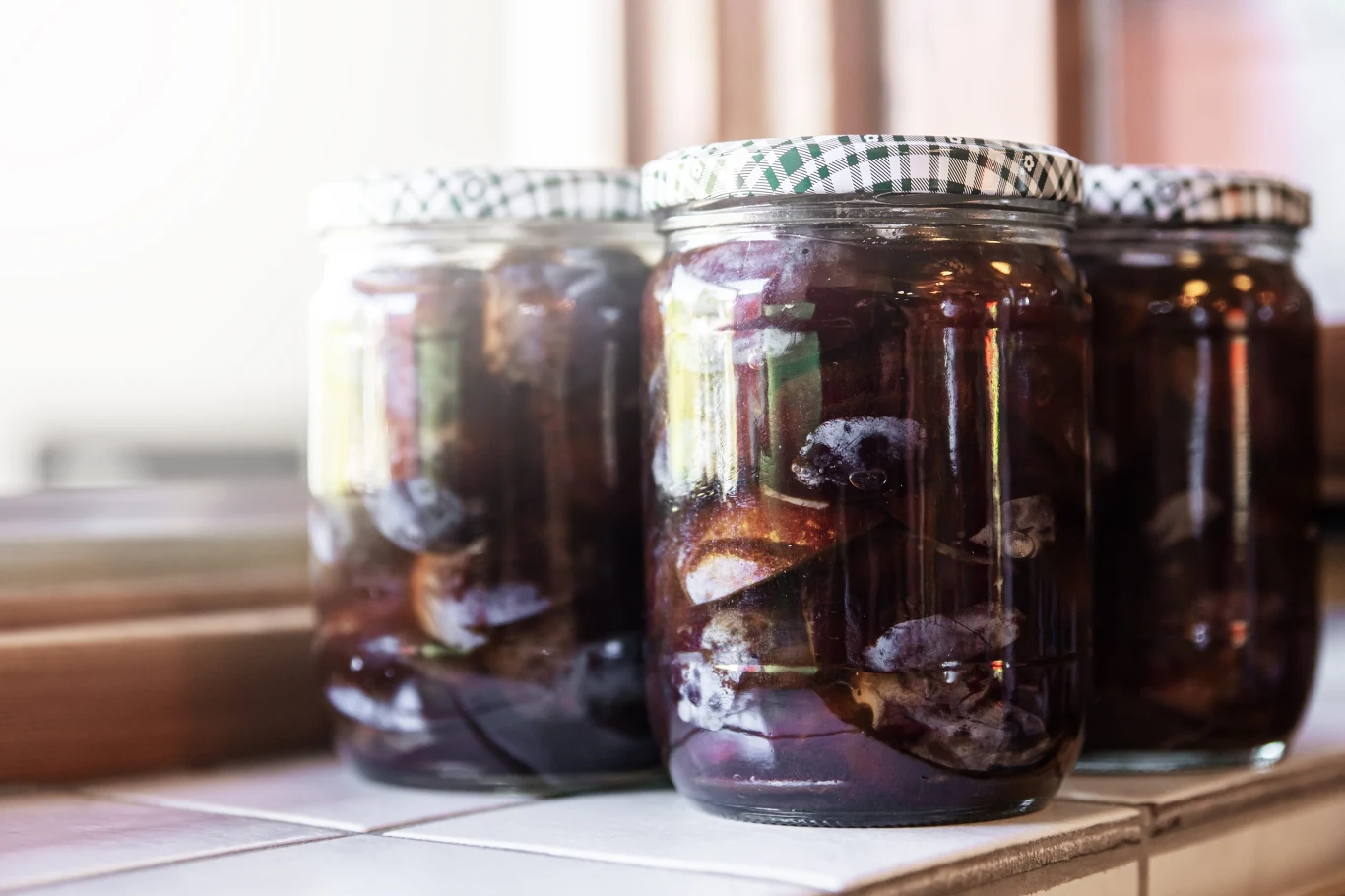 Jak zrobić śliwki w occie balsamicznym? Ten przepis pokochasz Słoiki z połówkami śliwek w zalewie, zamknięte zielono-białymi zakrętkami, stojące na białym blacie.