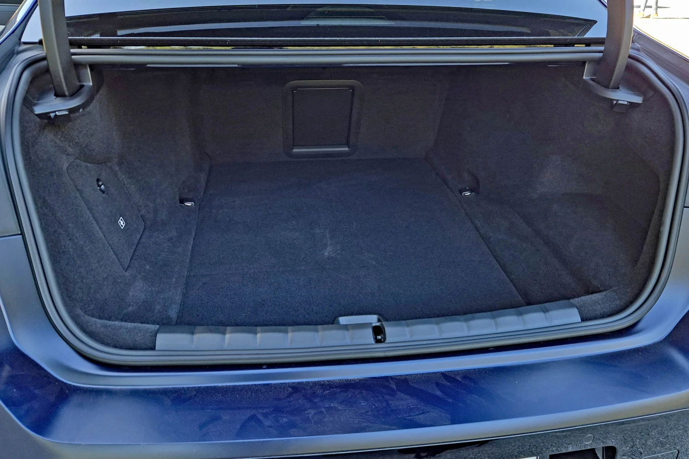 BMW serii 7 Pojemny, czysty bagażnik samochodu z równą podłogą, tapicerką w ciemnym kolorze i otworem w tylnej ściance ułatwiającym przewóz dłuższych przedmiotów.
